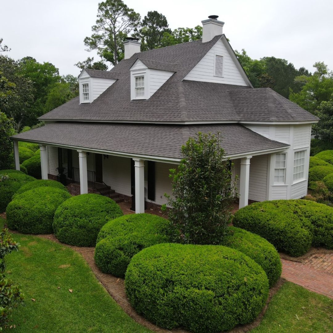 Aerial view of a white commercial building with a flat roof, surrounded by trees and a parking lot.