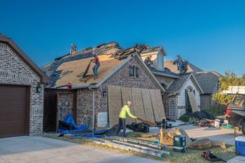 Roofers replacing a damaged roof on a house, working under a clear blue sky.
