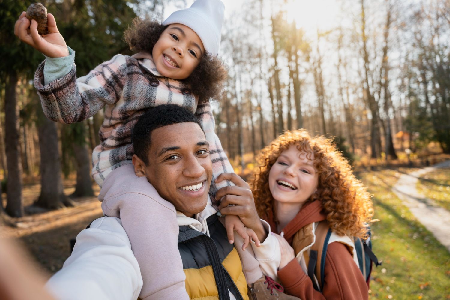 A man is carrying a little girl on his shoulders in a park.