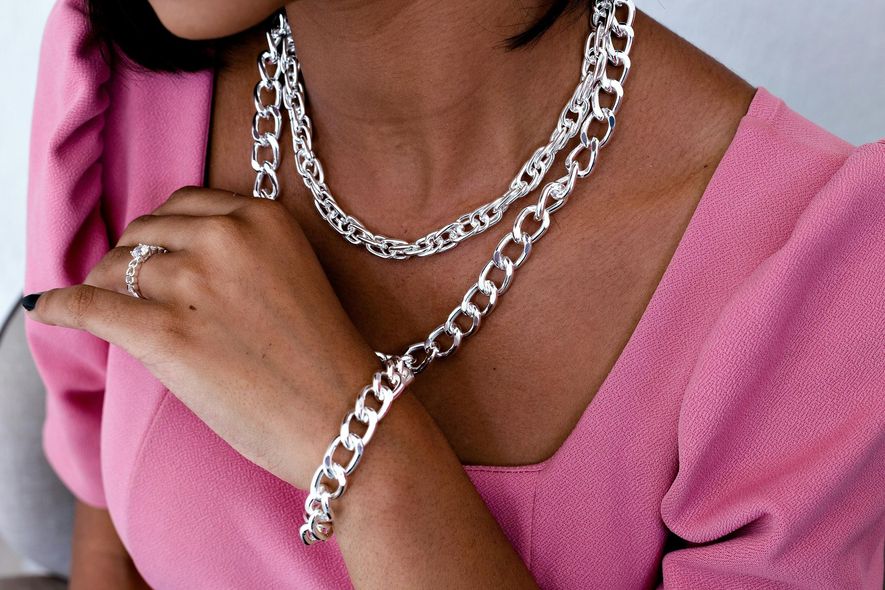 A woman wearing a necklace and bracelet is wearing a pink shirt