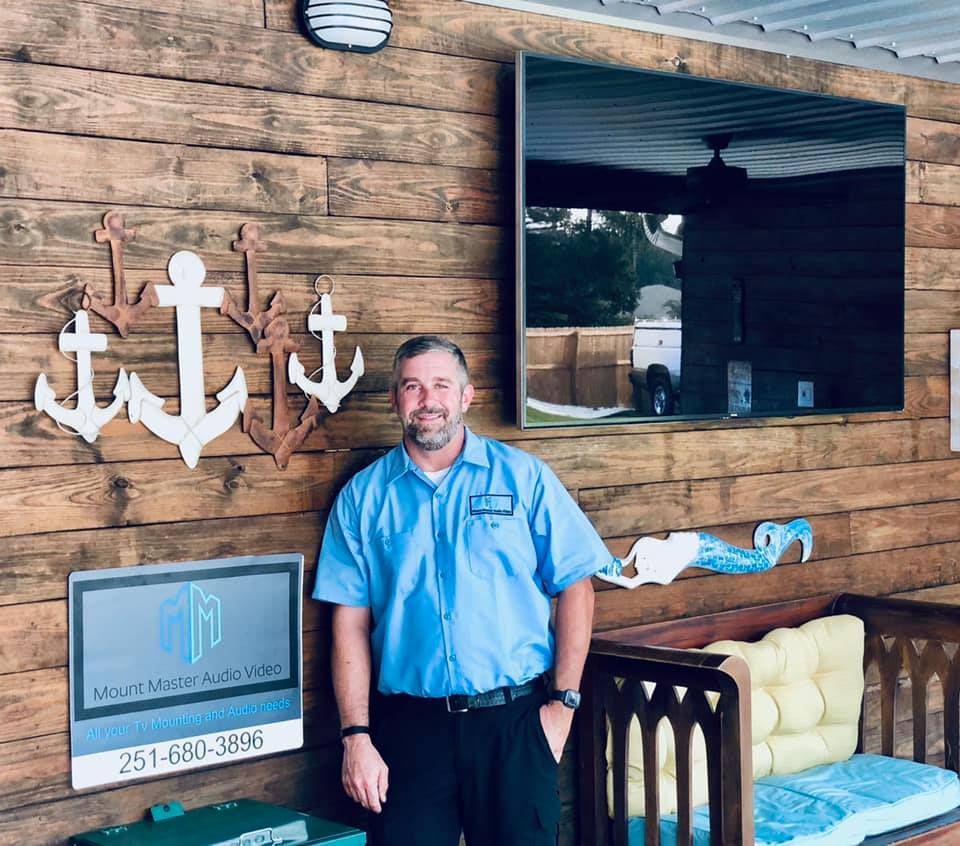 Man in blue shirt stands by wood wall with anchors and a mirror.