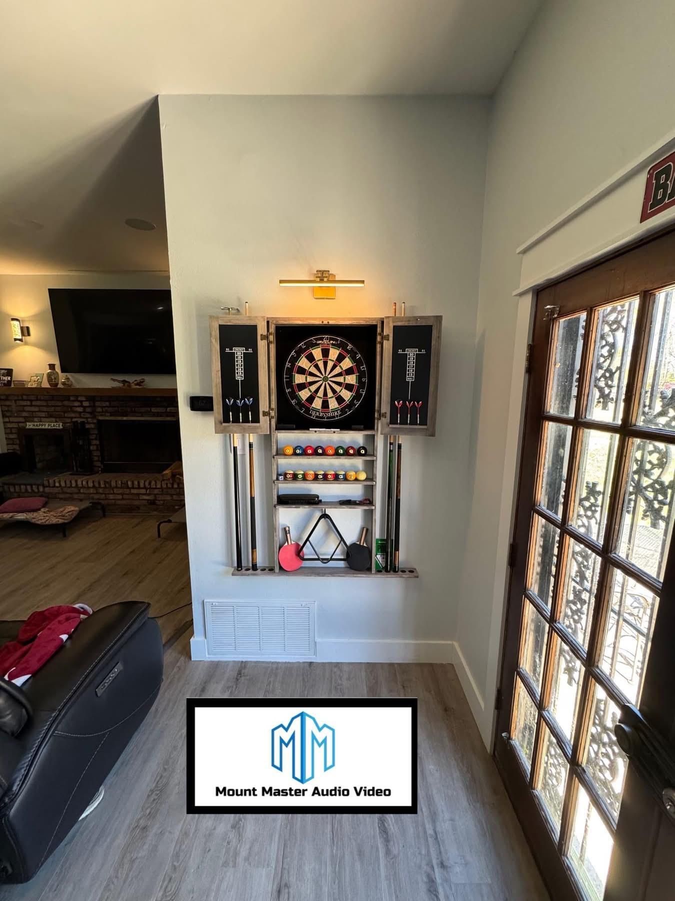 Dartboard set mounted on wall near a door. Cabinet includes accessories, surrounded by steel posts.