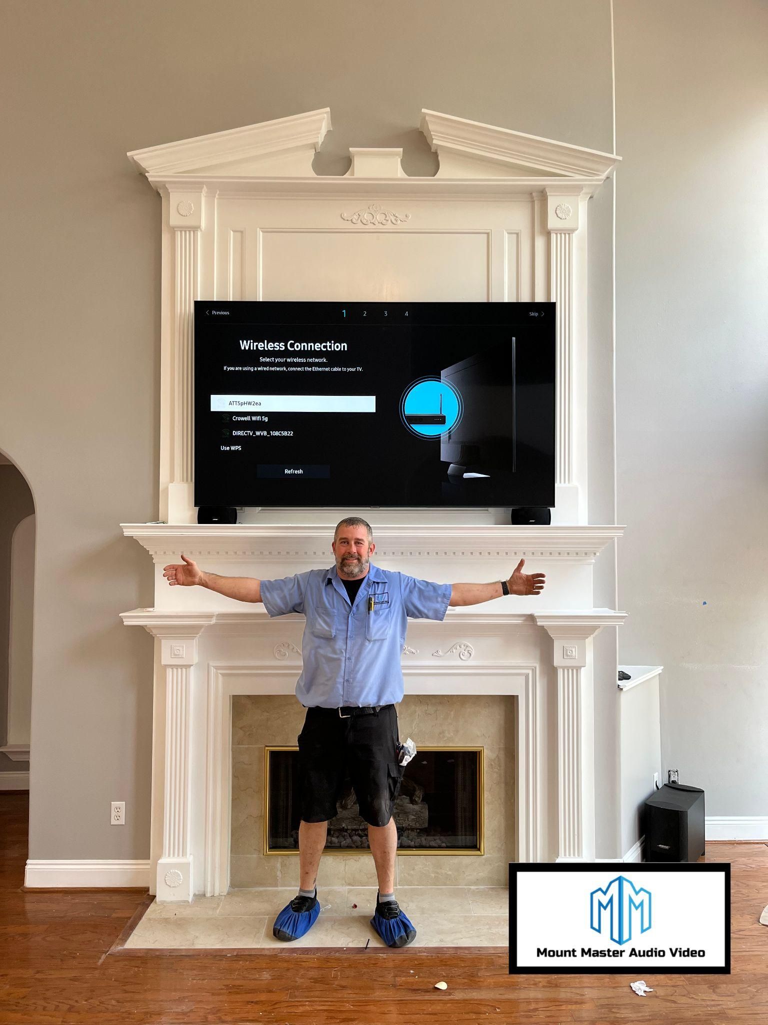 Man standing in front of a fireplace, with a mounted TV. He is smiling with arms outstretched.