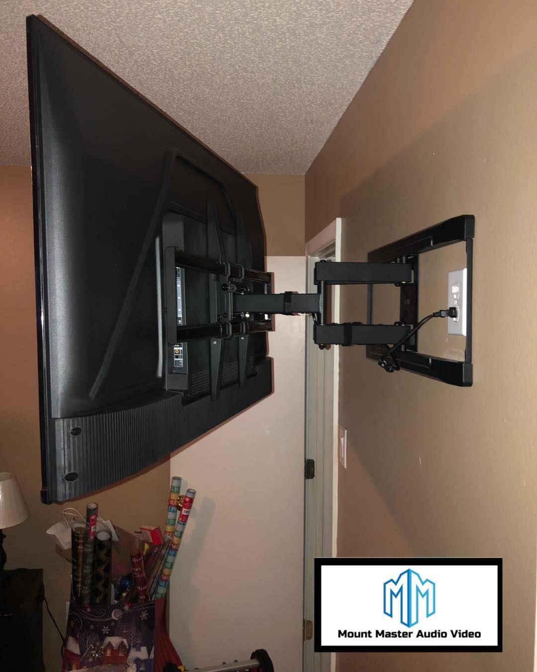 A large TV mounted on a wall, with a black articulating arm. The wall is beige, the door is in the background.