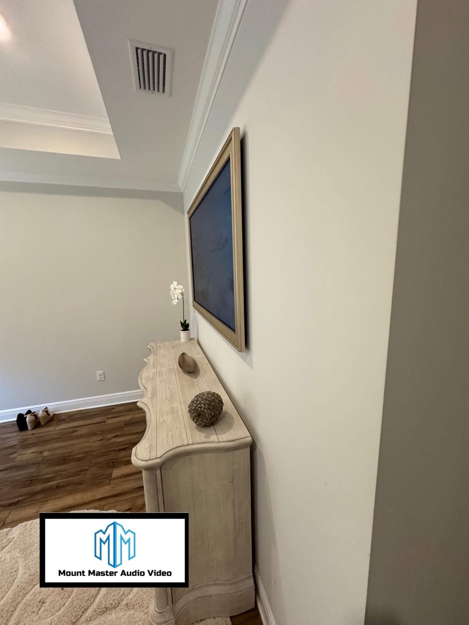A living room setup: TV mounted above a distressed white cabinet, wood floor, white walls.