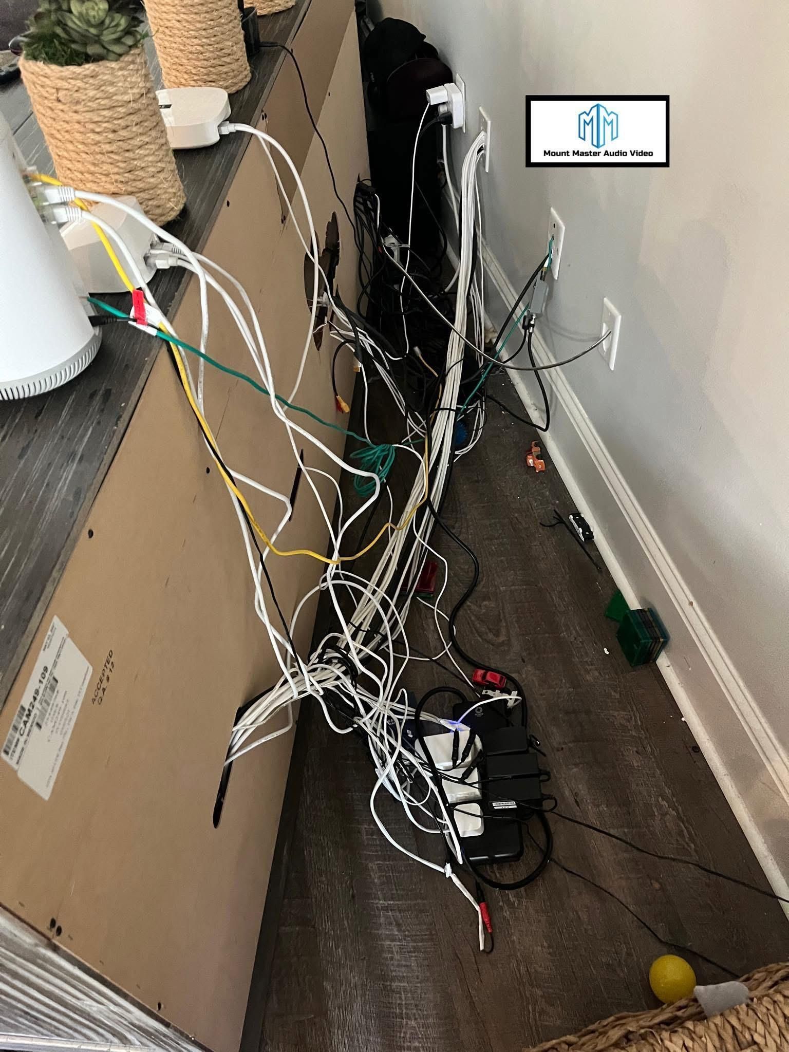 Tangled white and black wires behind a brown cabinet and against a white wall; visible power strip and floor.