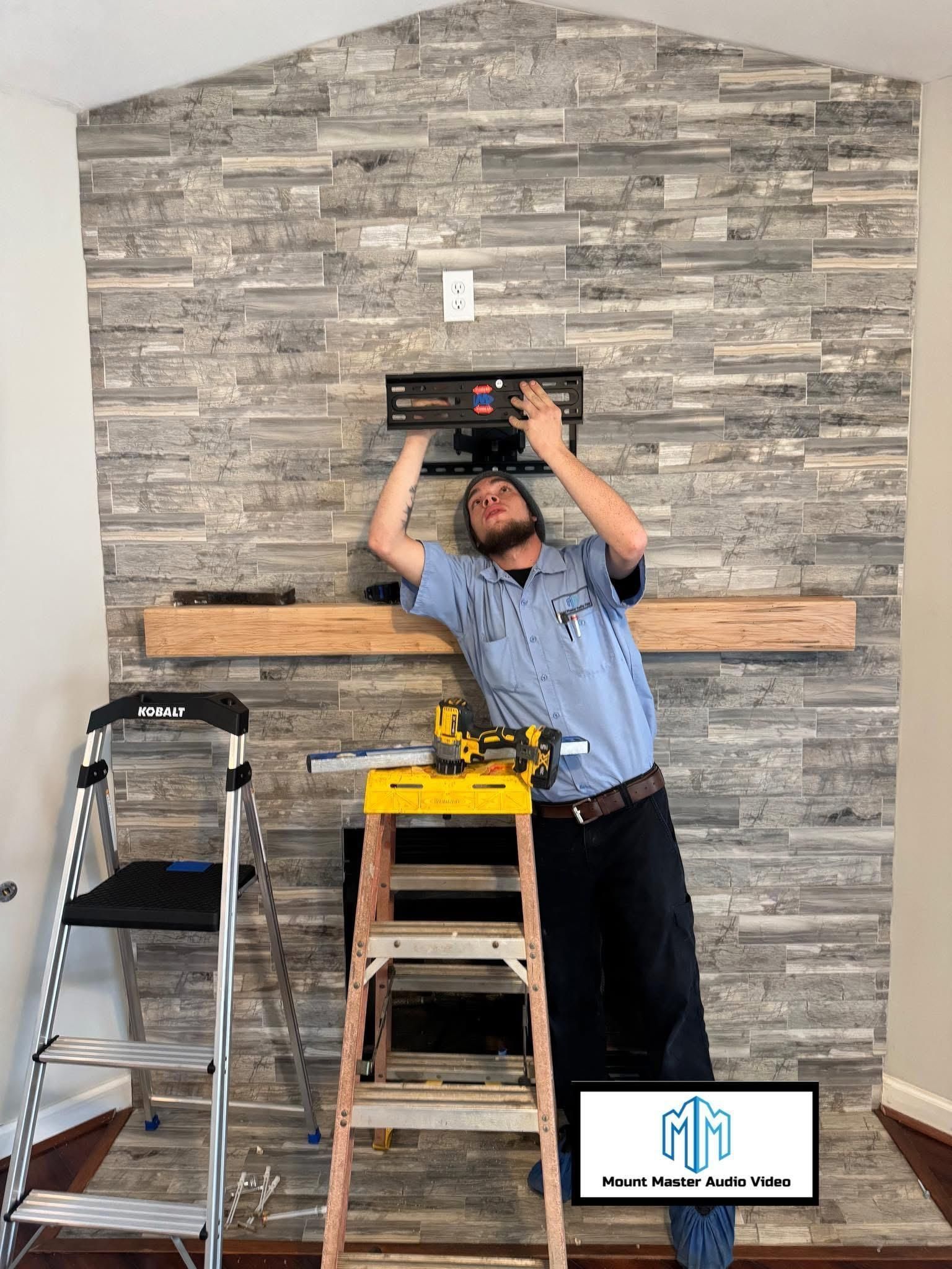 Man installing TV mount on a stone fireplace, using a ladder.
