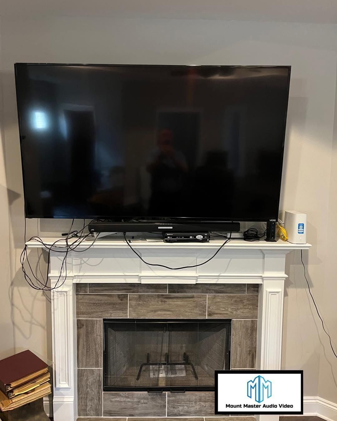 Large TV mounted above a fireplace with tangled wires and a sound bar.