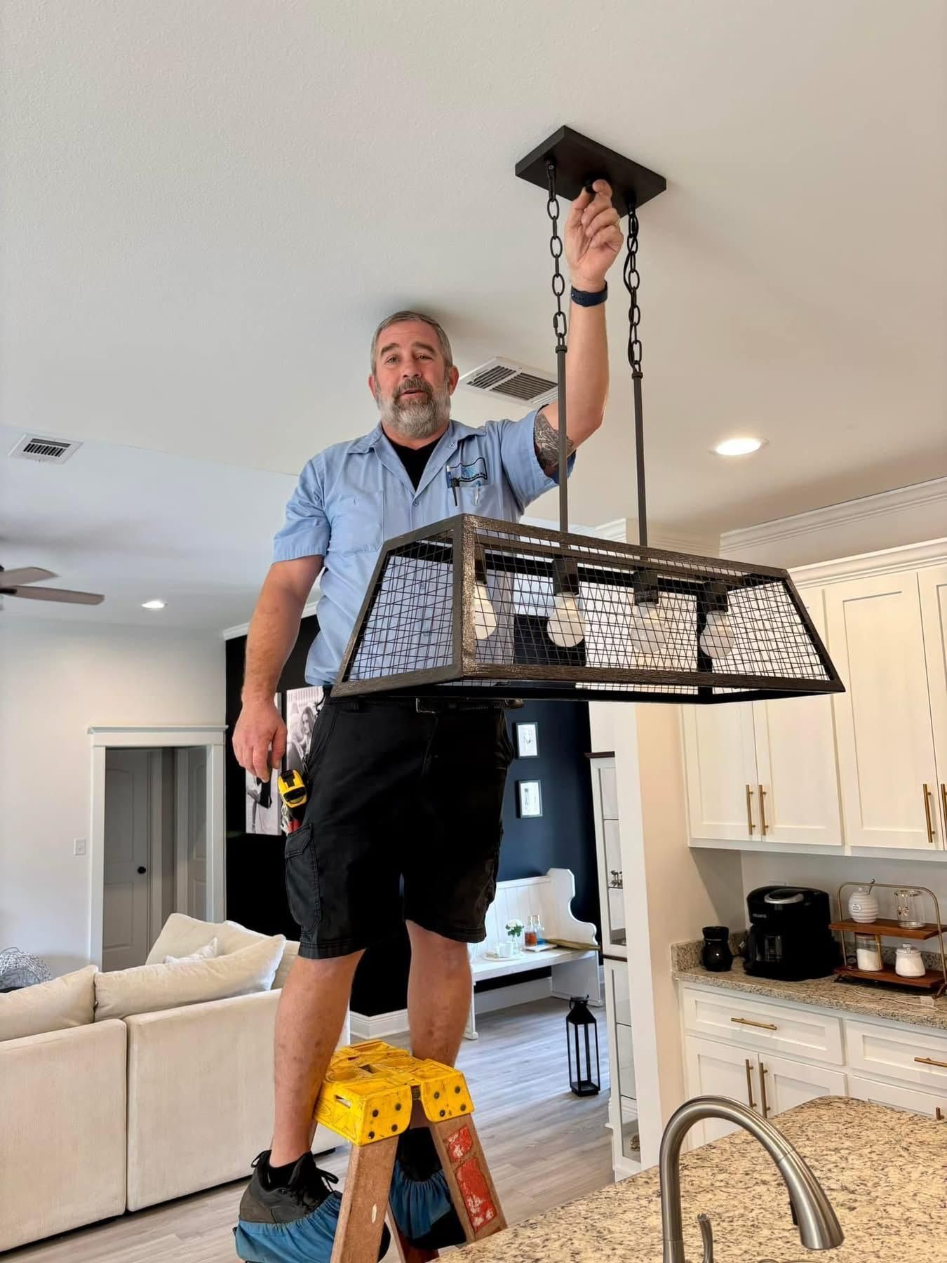 Man on stepladder installing a light fixture in a kitchen.