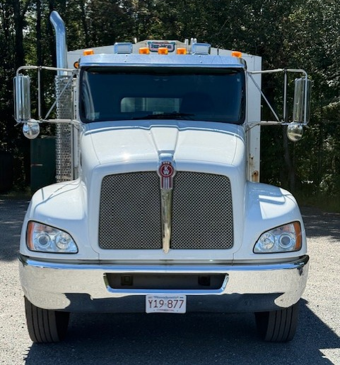 White Kenworth semi-truck with chrome accents, parked in front of trees. White Kenworth semi-truck with chrome accents, parked in front of trees.