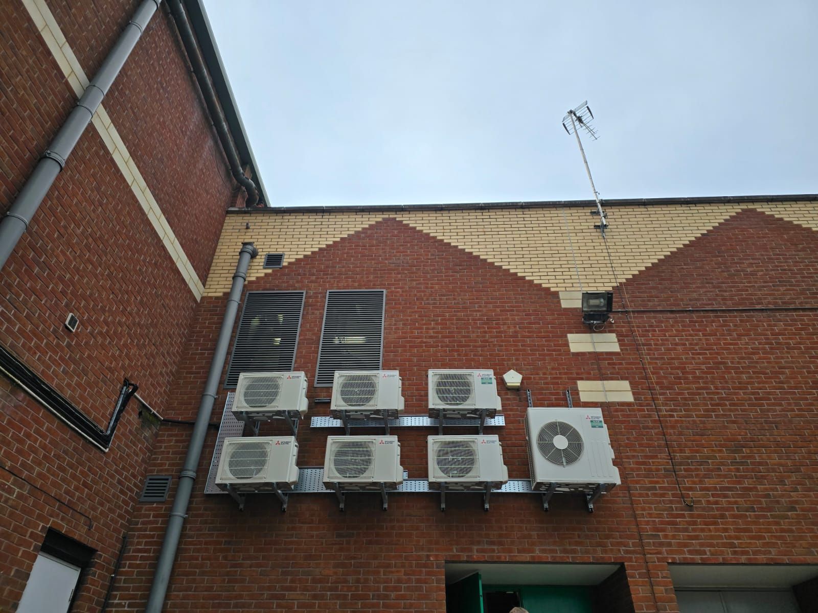 Brick building wall with six outdoor AC units and a rooftop antenna under a blue sky