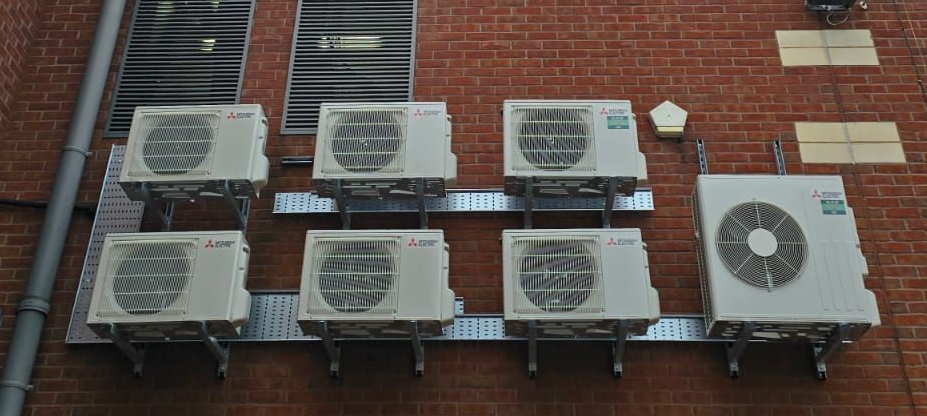 Rows of outdoor AC units mounted on a brick wall under a fire escape staircase