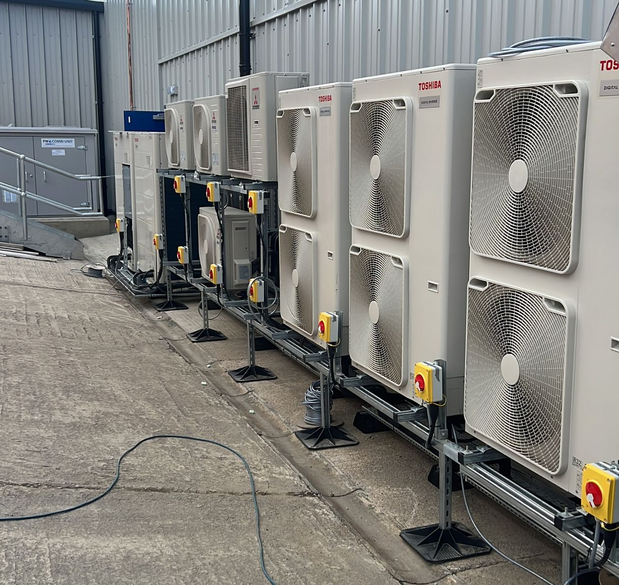 Row of outdoor industrial HVAC units beside a metal building, with vents and control panels on gravel.