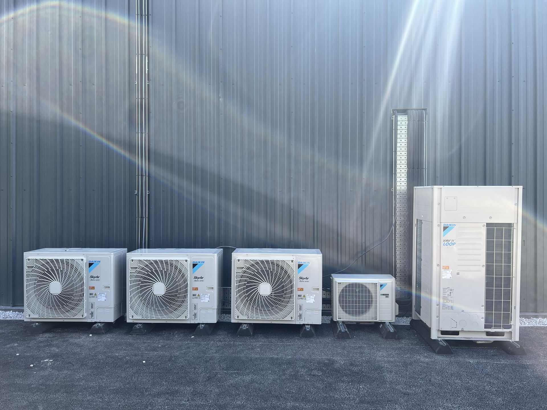 Industrial HVAC units lined up against a corrugated metal wall on a paved surface