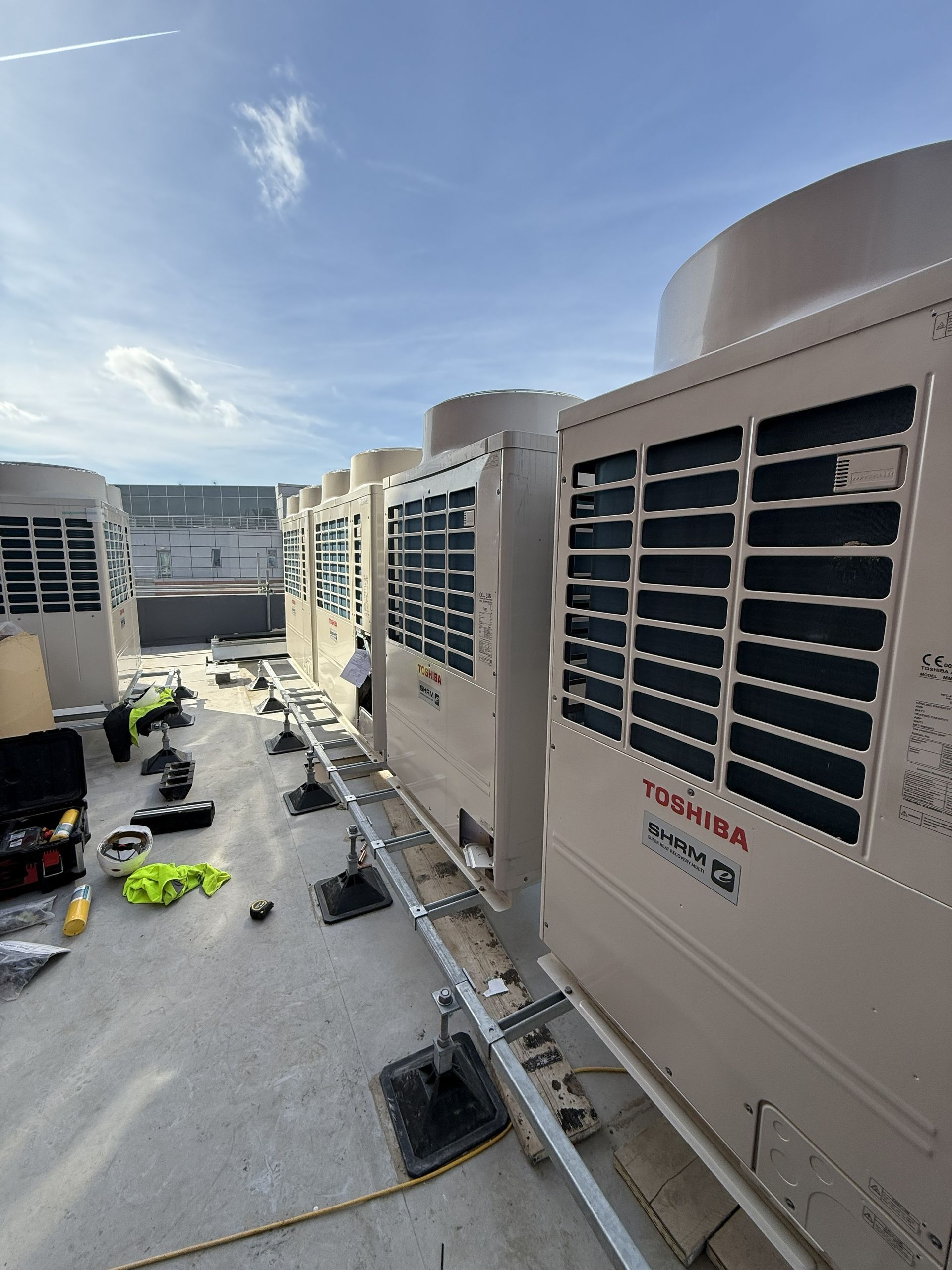 HVAC units on a rooftop walkway beside a building under a clear blue sky