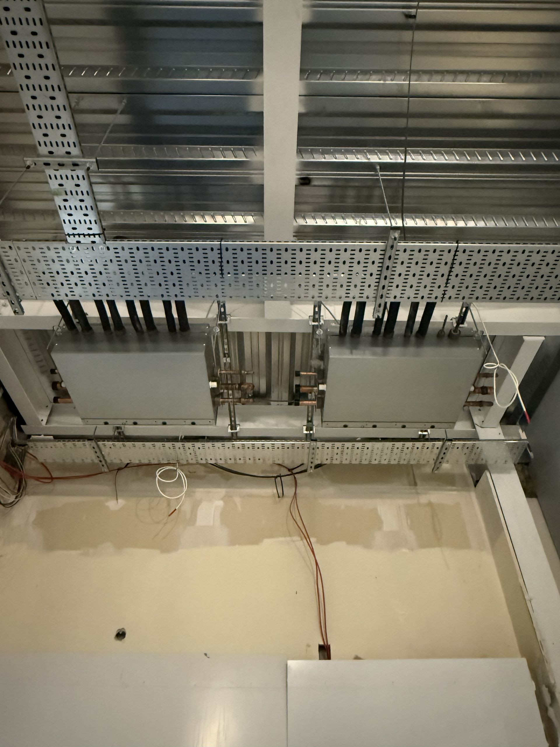 Ceiling with exposed metal beams, cable trays, and electrical boxes above a beige wall.
