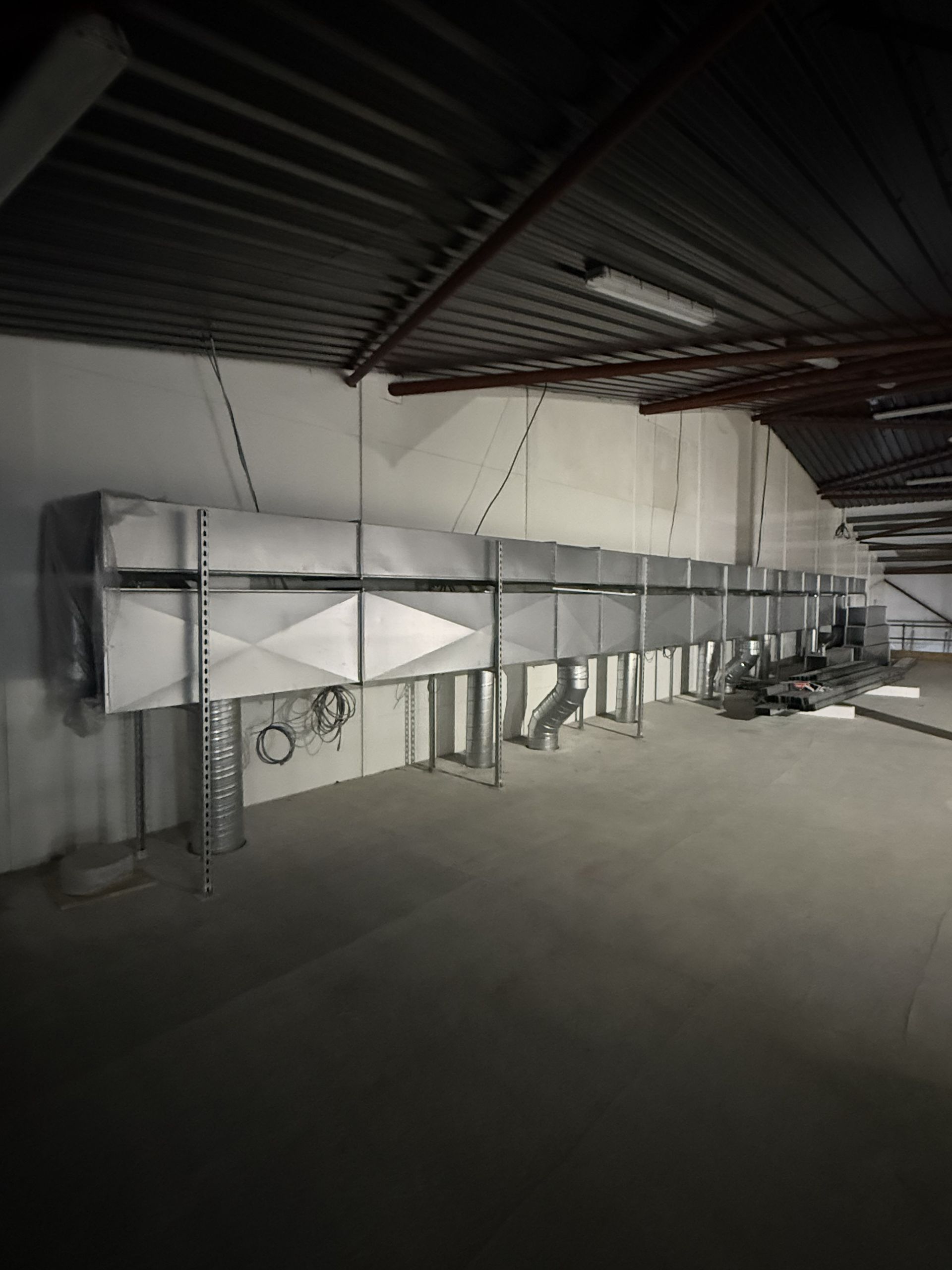 Industrial ceiling ductwork and metal supports in a dim warehouse-like interior.