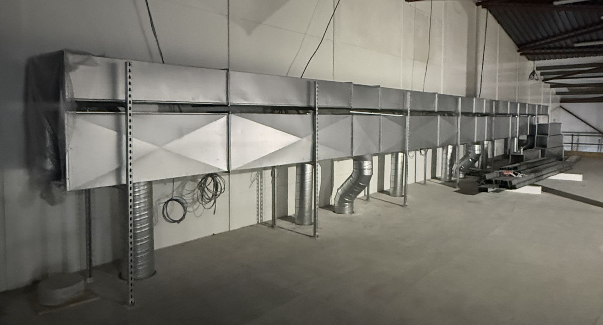 Large industrial HVAC duct system installed along a warehouse wall with metal supports and vents