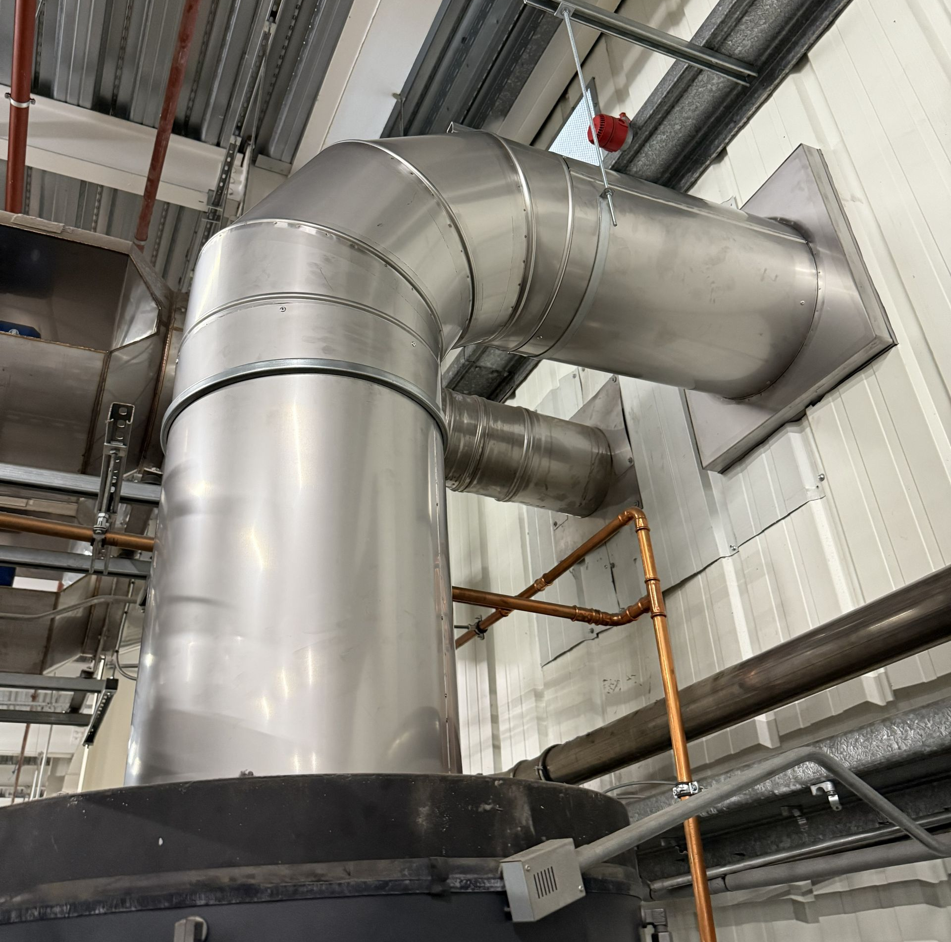Large silver industrial ductwork with curved metal pipes inside a warehouse or factory ceiling