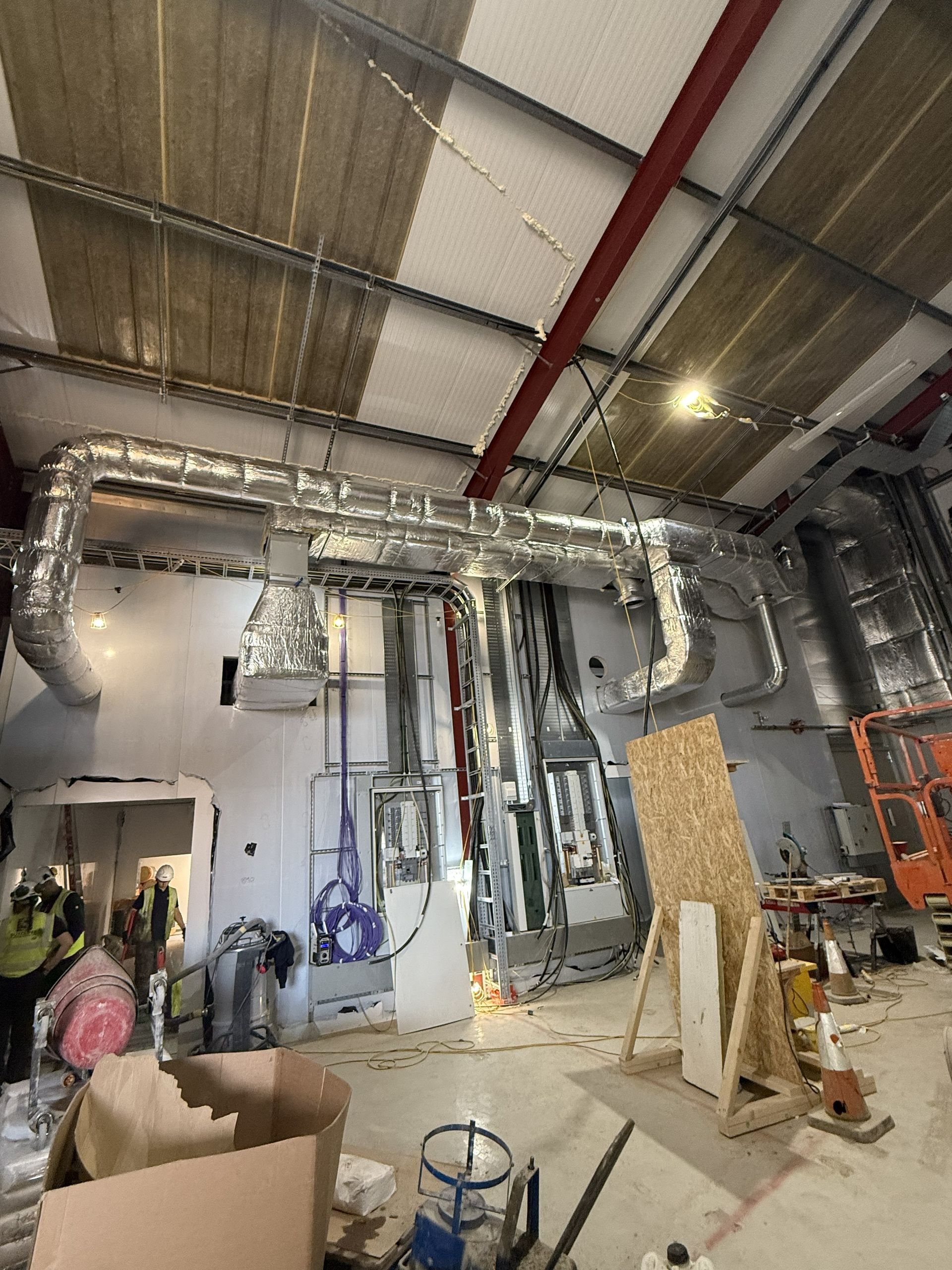 Industrial workshop with exposed silver ductwork, tools, and equipment under a high ceiling.
