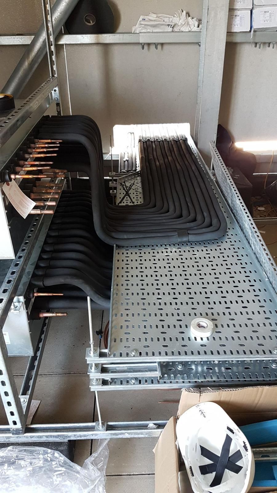 Industrial conveyor and perforated metal platform with stacked black cable trays in a warehouse.
