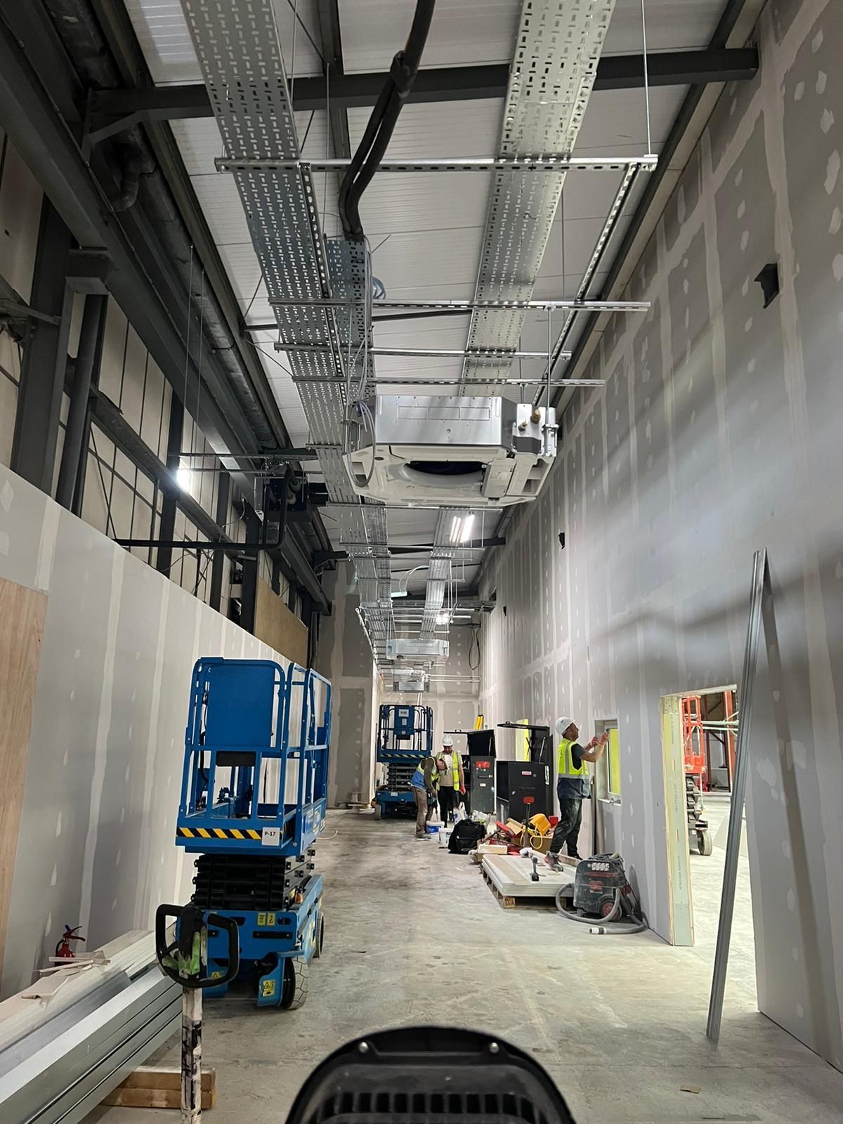 Industrial hallway with a tall ceiling, scaffolding, and workers near equipment