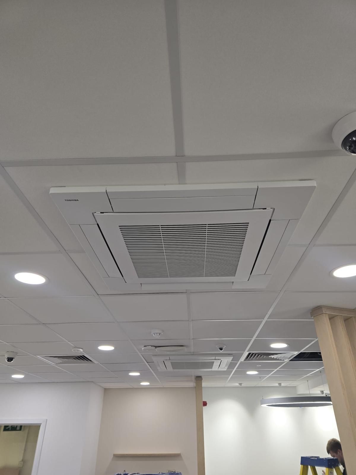 Office ceiling with white square air vent, recessed lights, and a partial view of a person at right