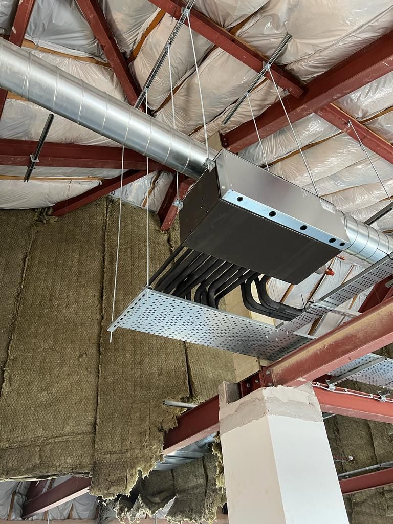 Industrial HVAC unit suspended from a red steel ceiling in an unfinished warehouse space