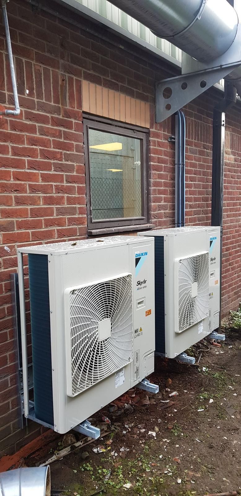 Two white outdoor HVAC units mounted beside a brick building under a metal awning