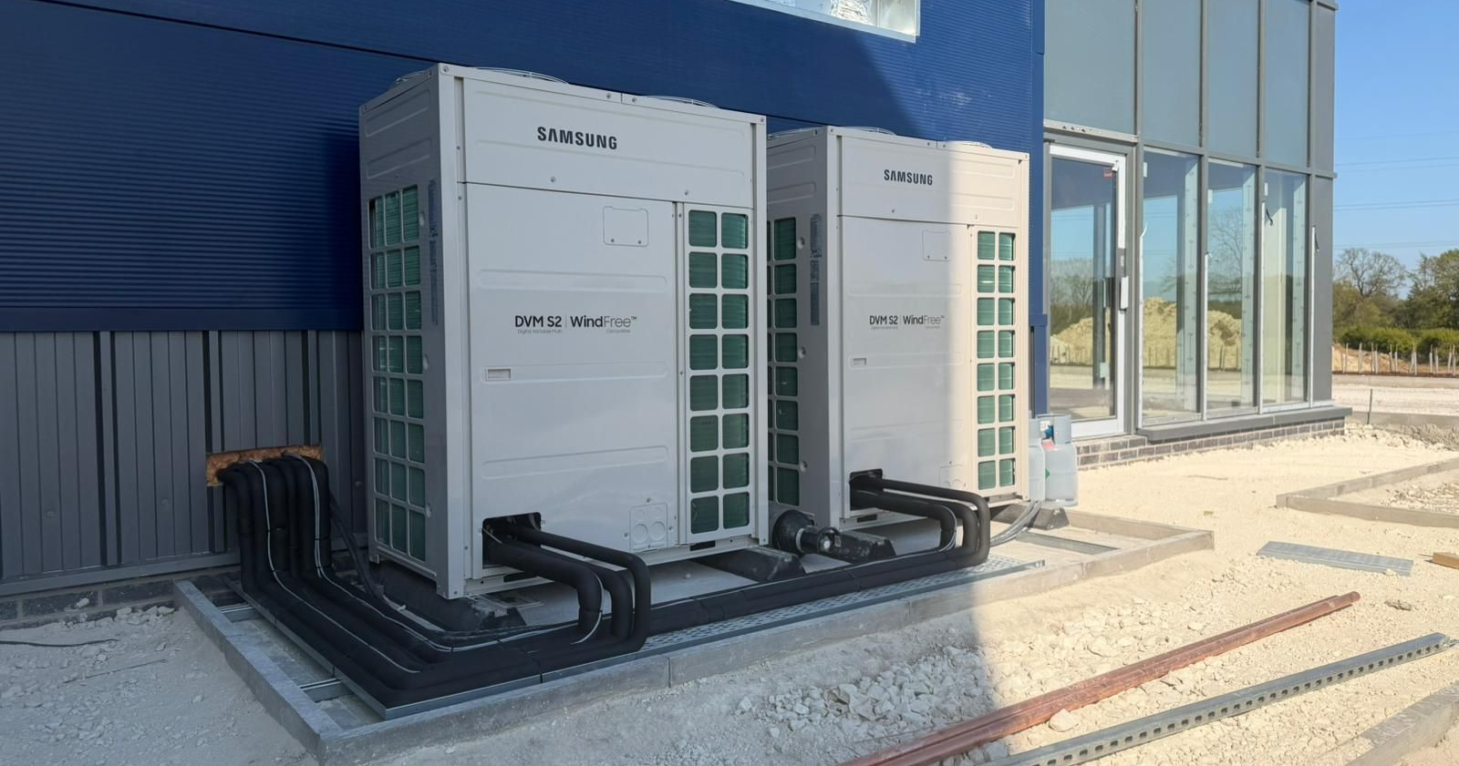 Outdoor industrial HVAC units beside a blue building with glass windows and connected black pipes