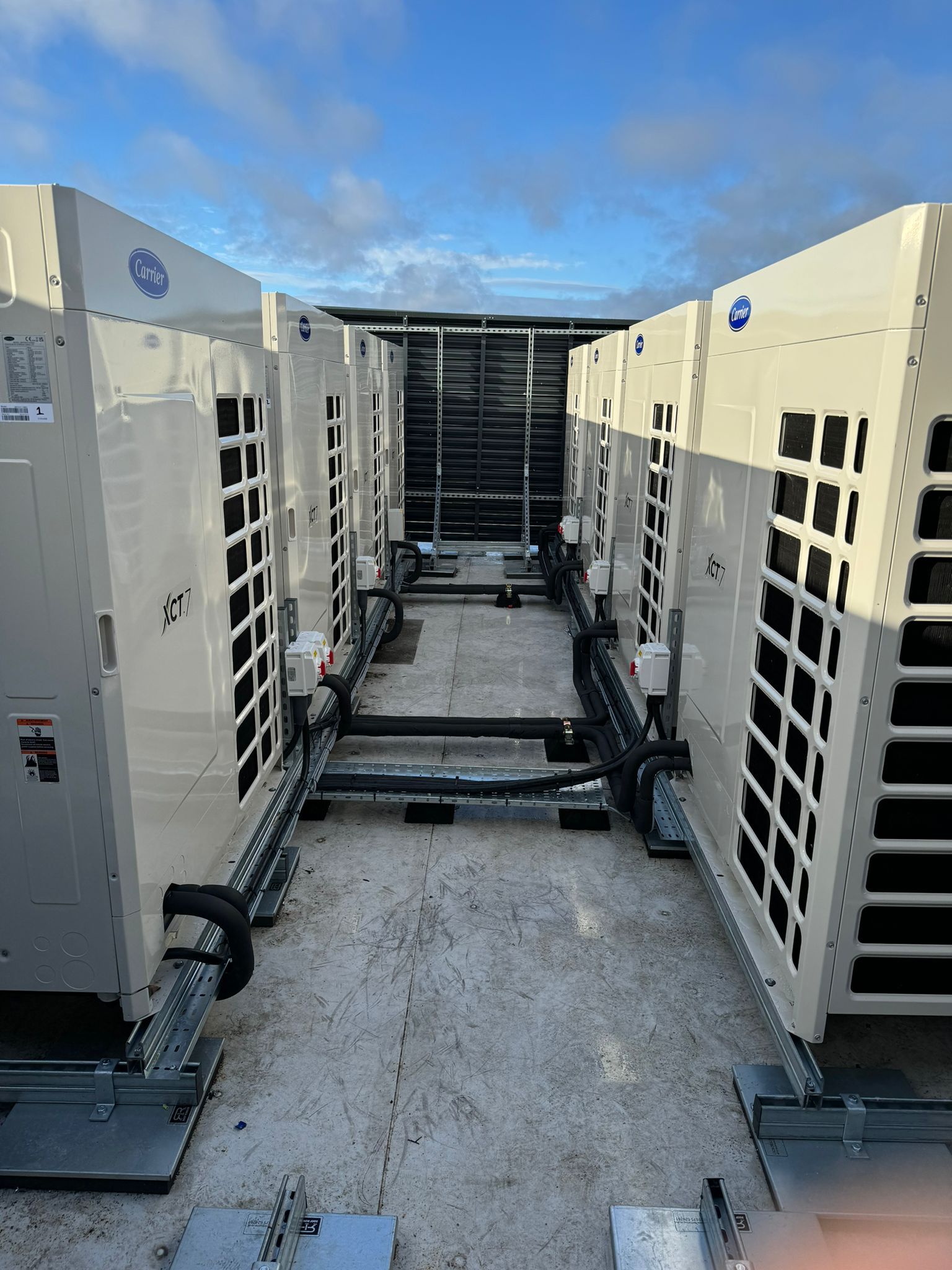 Outdoor view of large cream-colored HVAC units lined in a narrow service corridor under a blue sky