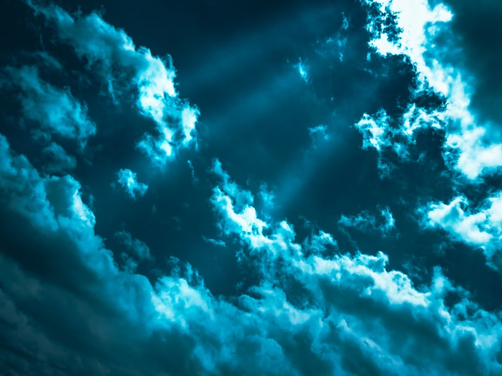 The sun is shining through the clouds in a dark blue sky.