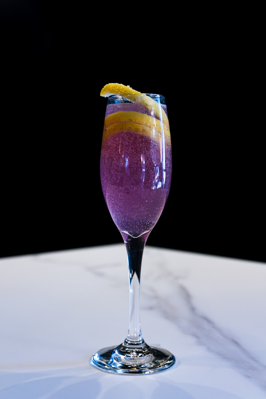 Closeup of Six-Mile Ordinary Cocktail With People Sipping Their Drinks in the Background. 