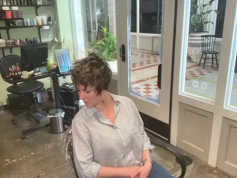 Woman seated in a salon lobby, looking down beside glass doors and a workspace