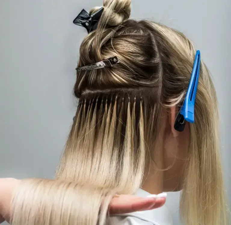 Hair stylist sectioning blonde hair with clips for dyeing, showing dark roots and bleached ends.