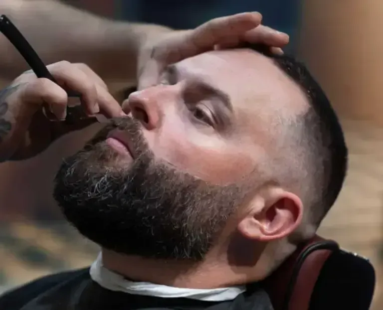 Bearded man getting a straight razor shave in a barber chair