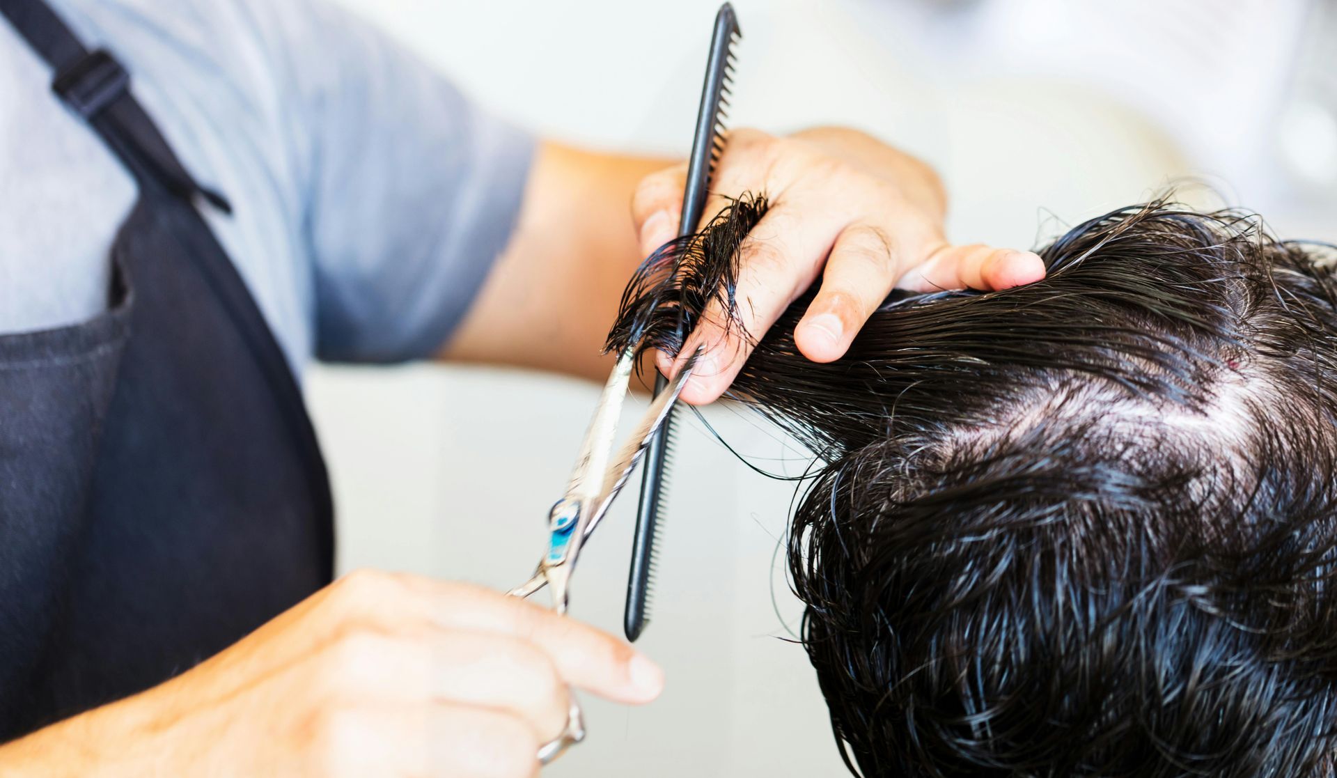 Hairdresser trimming wet hair with scissors and comb at a salon