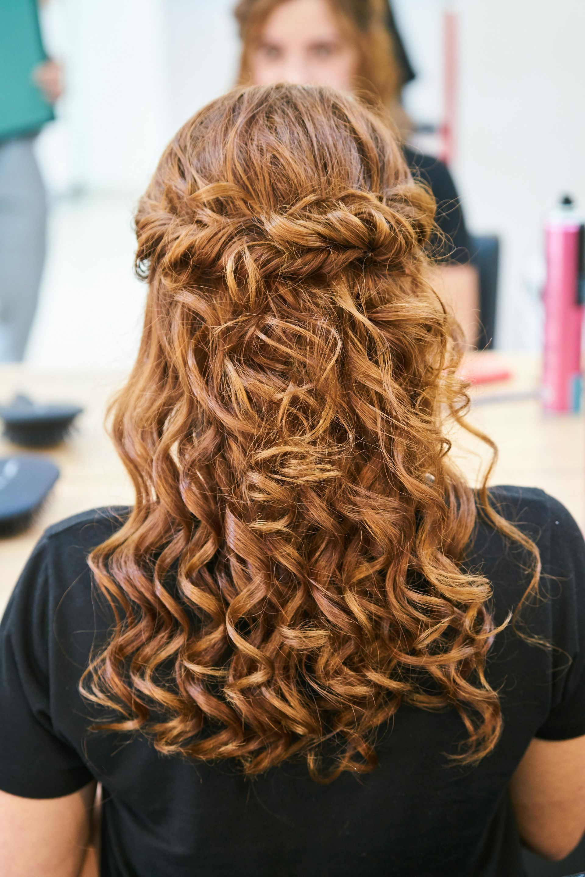 Curly brown hair styled half-up in a salon mirror view