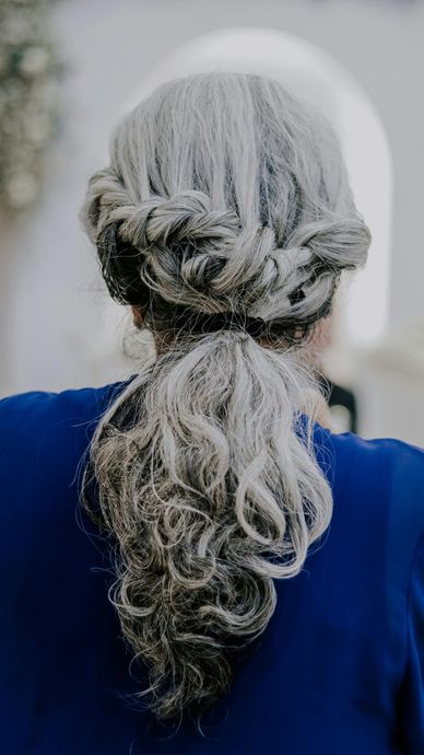 Back view of a person with long gray braided hair against a blurred light background