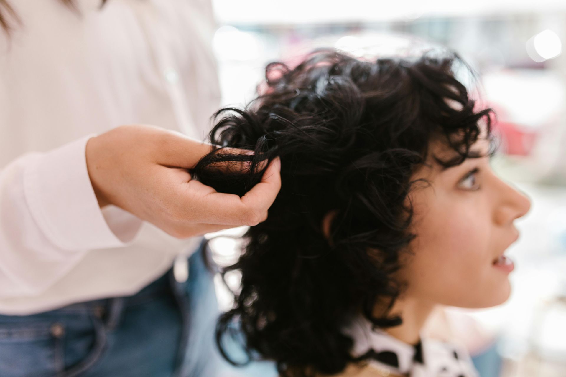 Stylist curling a client’s dark hair in a bright salon