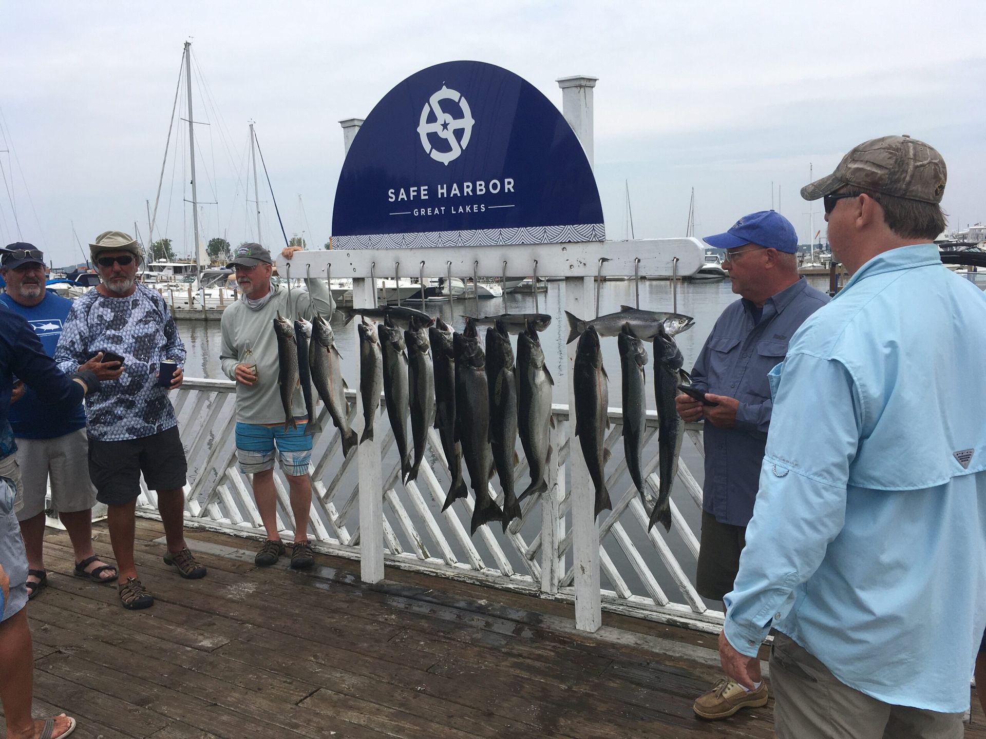 Men on a dock display caught fish. Blue Harbor sign in background.