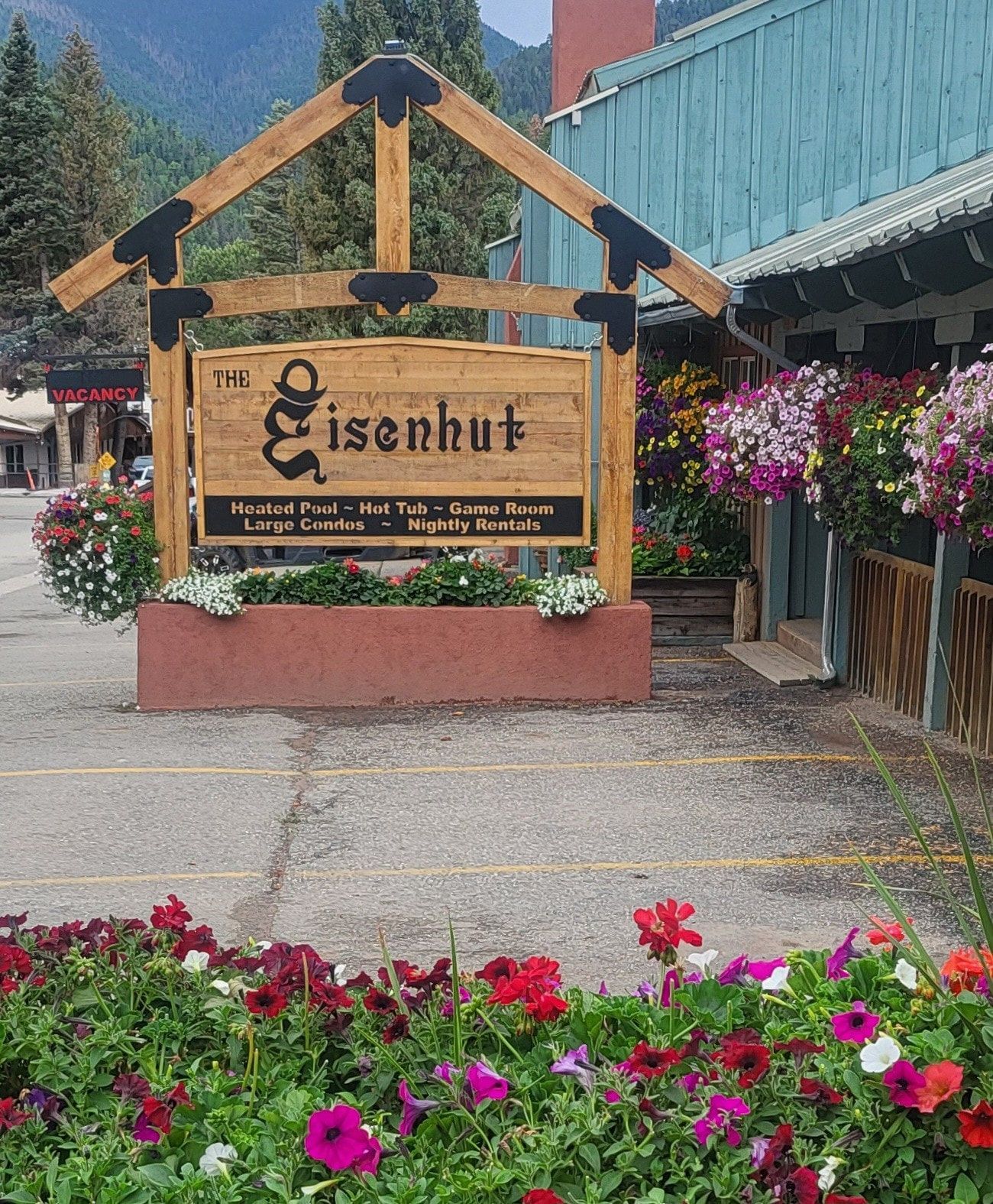 Wooden “Eisenhut” sign at a garden center with hanging flowers and bright blooms in front