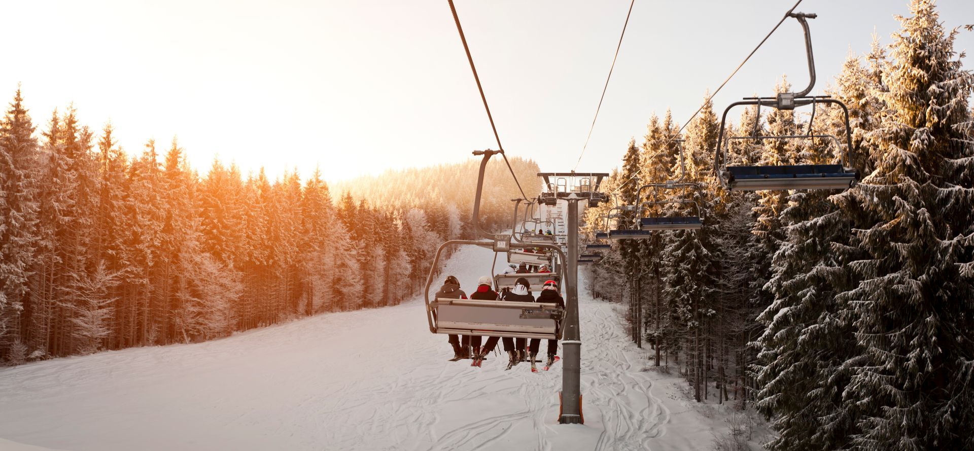 Ski lift over snow-covered forest at sunset with warm orange light