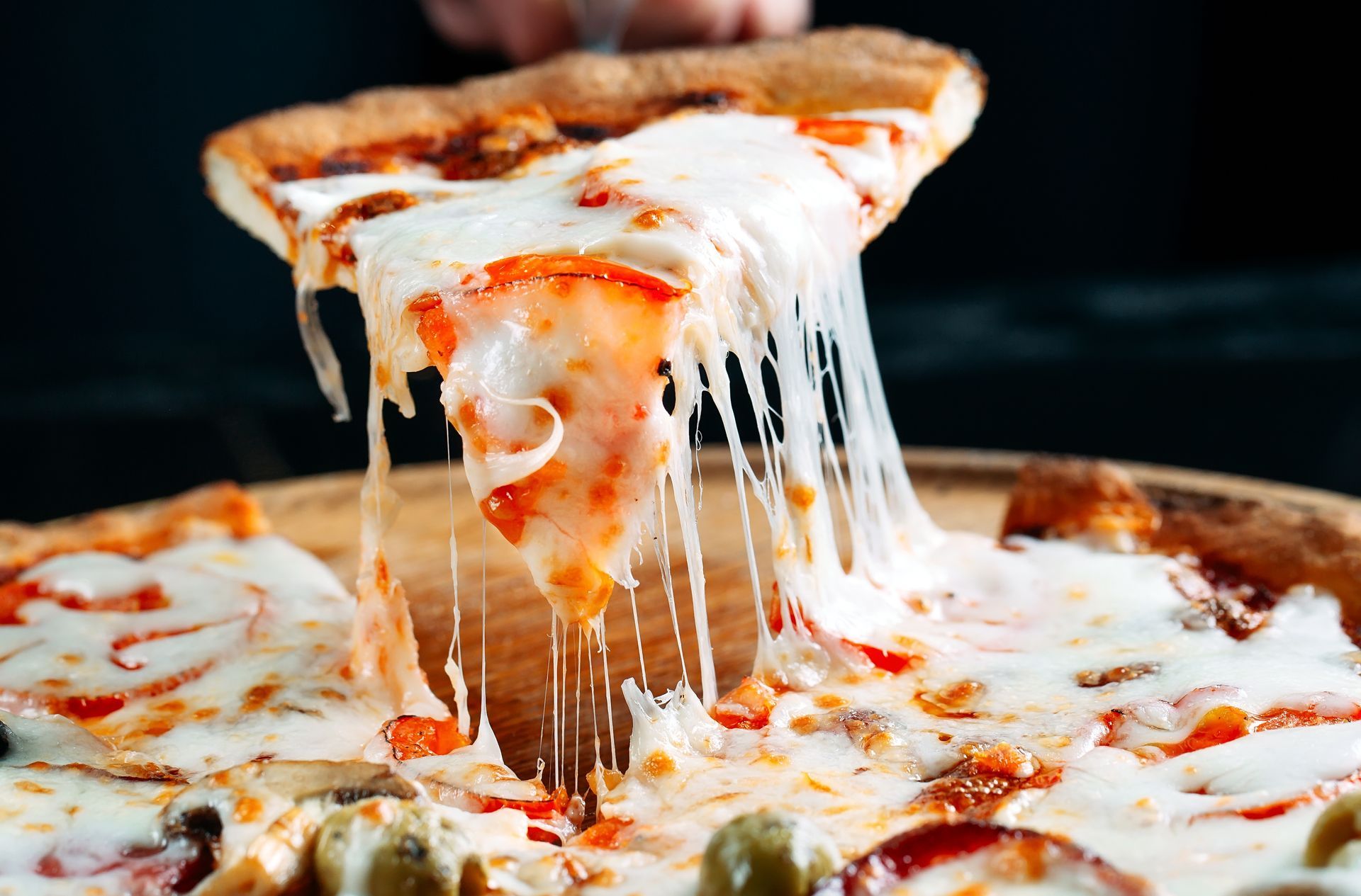 Close-up of a cheesy pizza slice being lifted, with melted cheese stretching from the pie