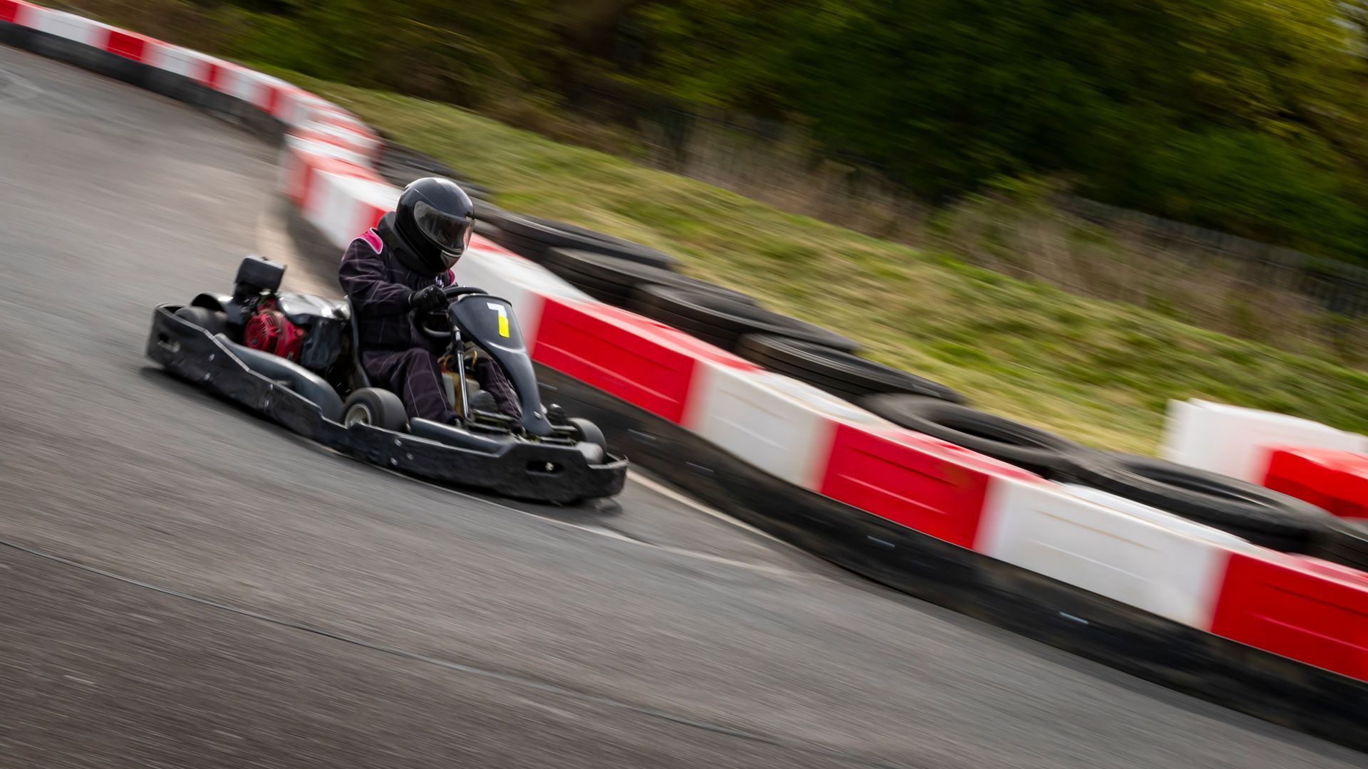 Go-kart racer speeding through a curve beside red-and-white barriers on a track