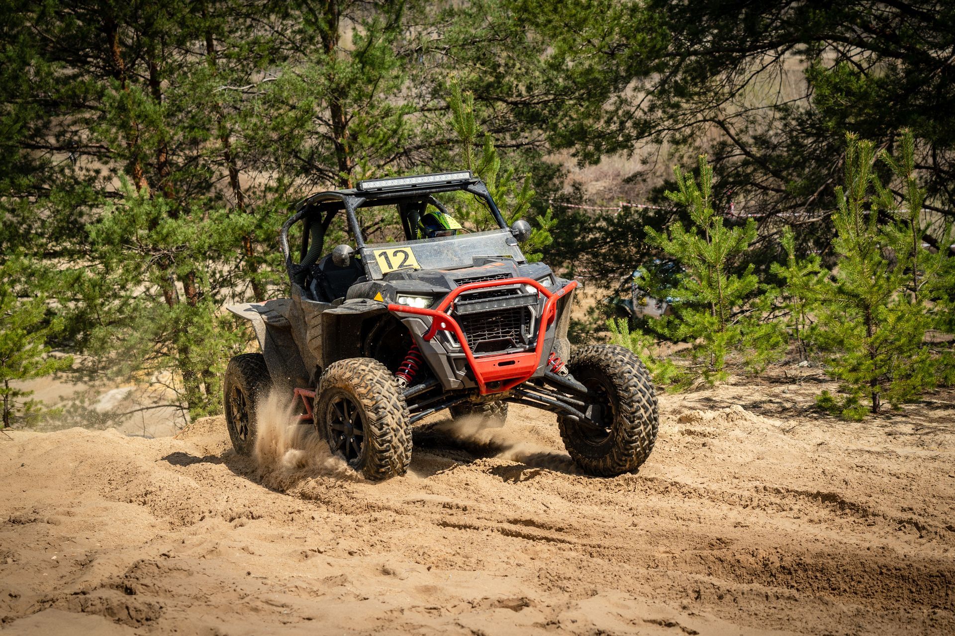 ATV racing through a sandy trail with trees in the background