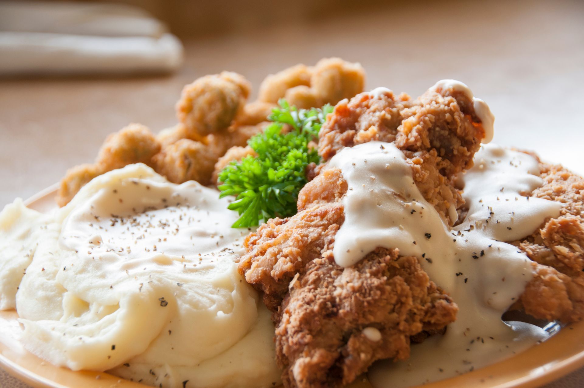 Fried chicken and mashed potatoes smothered in white gravy, garnished with parsley on a plate