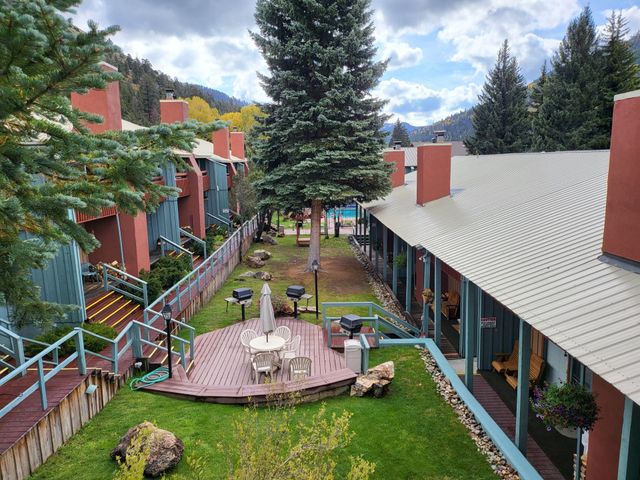 Courtyard between red-roofed buildings with a central deck, patio furniture, lawn, and tall evergreen trees