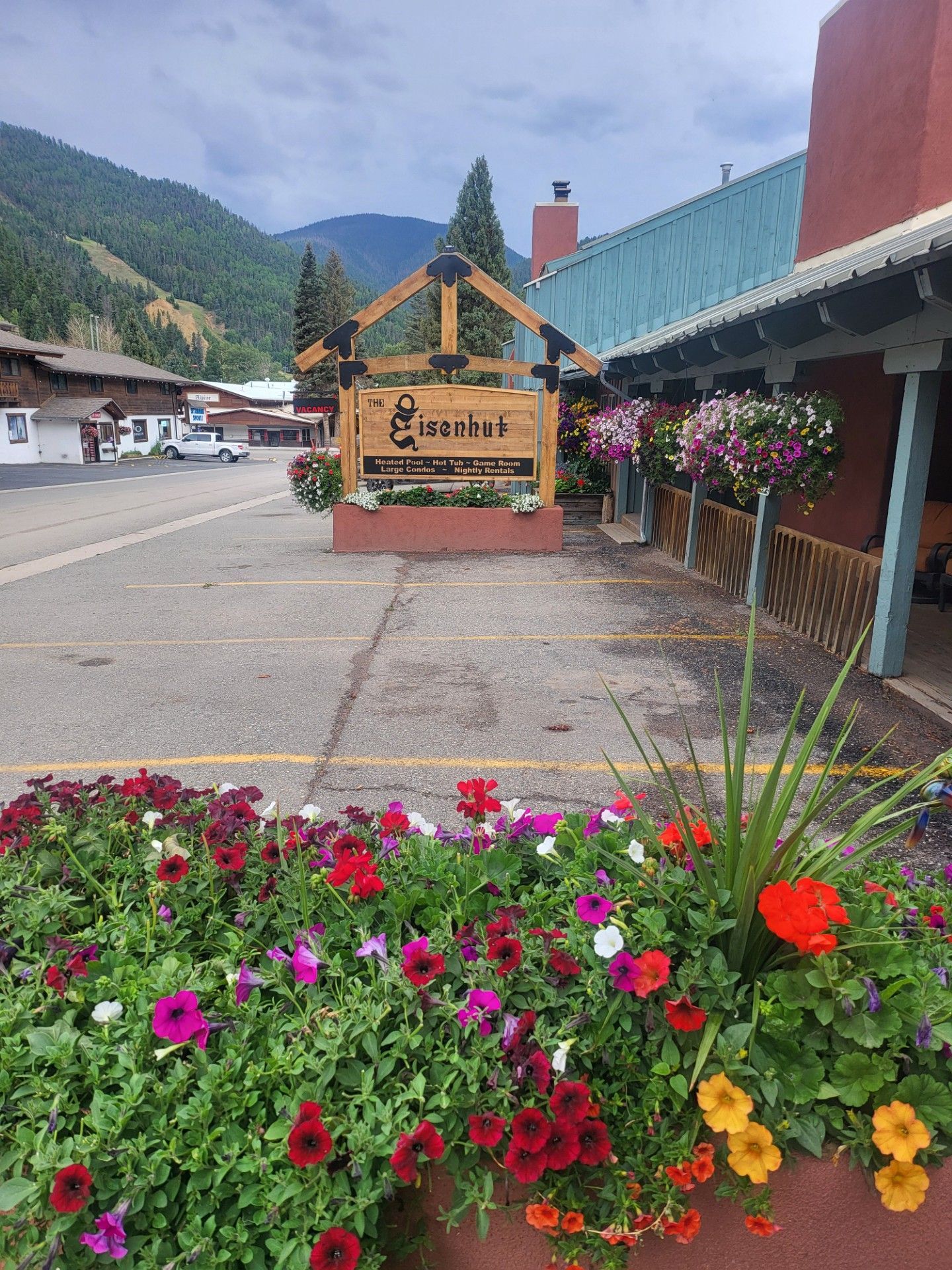Flower bed with red, pink, and yellow blooms beside a village street and mountain cabins