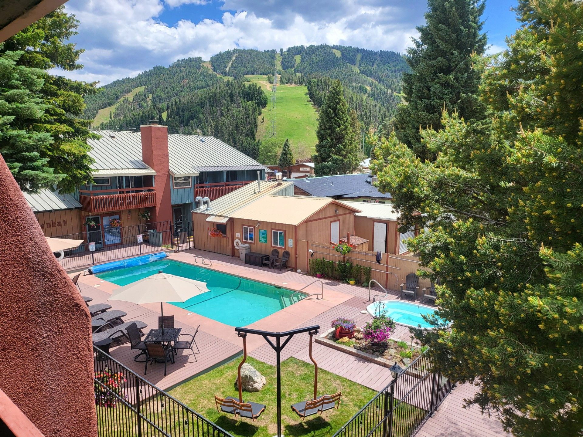 Mountain resort pool area with turquoise pools, lounge chairs, and forested ski slopes in the background